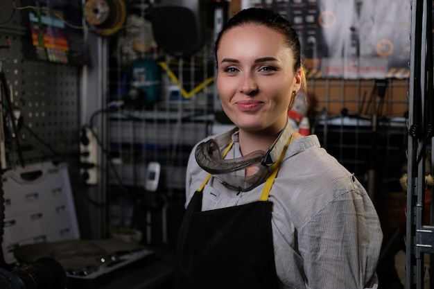 Ritratto di una bella donna bruna sorridente che indossa abiti da lavoro e grembiule, in piedi in un'officina