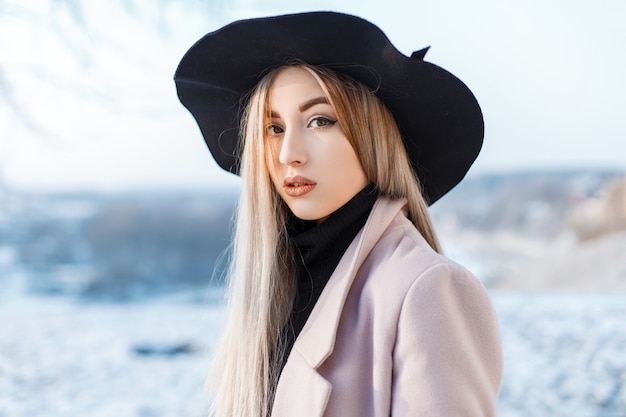 Ritratto di una bella donna carina con trucco naturale con pelle pulita in un elegante cappello elegante in un cappotto rosa in un campo da golf a maglia vintage. Ragazza sensuale. Avvicinamento.