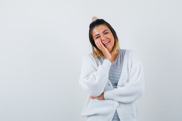 Ritratto di una bella donna che si appoggia la guancia a portata di mano in maglietta, cardigan e sembra gioiosa