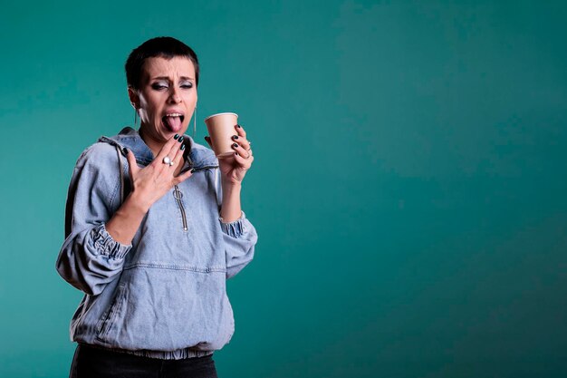 Ritratto di una bella donna che tiene in mano una tazza di caffè che beve una bevanda calda che fa un'espressione negativa