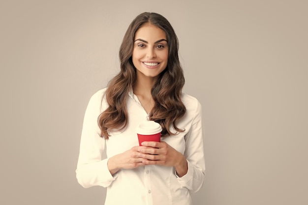 Ritratto di una bella donna che tiene una tazza di caffè da asporto isolata su sfondo grigio