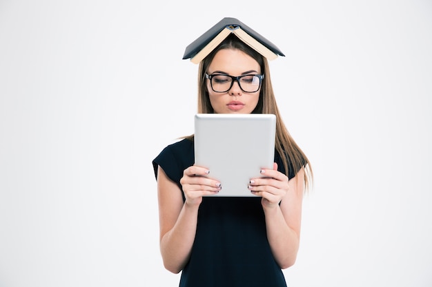 Ritratto di una bella donna che utilizza un computer tablet con un libro sulla testa isolata