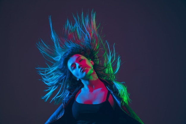 Ritratto di una bella donna con i capelli che soffiano su uno sfondo scuro dello studio con una luce al neon colorata