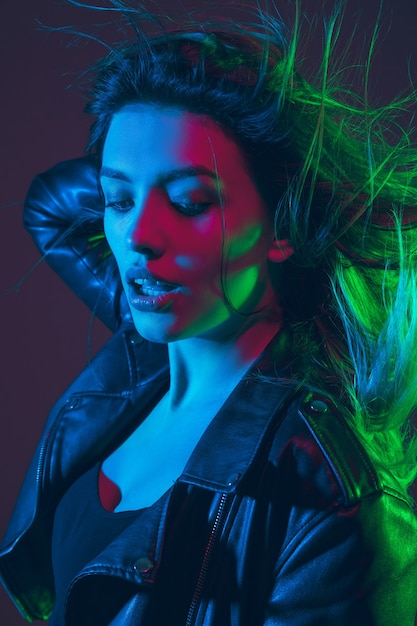 Ritratto di una bella donna con i capelli che soffiano su uno sfondo scuro dello studio con una luce al neon colorata