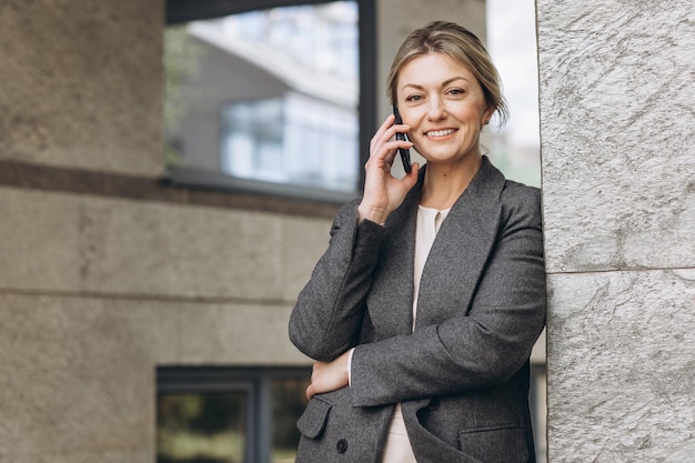 Ritratto di una bella donna d'affari matura sorridente e parlando al telefono sullo sfondo urbano moderno