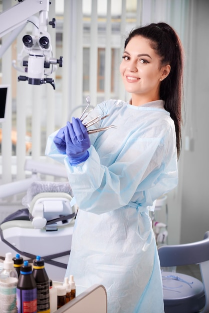 Ritratto di una bella donna dentista che tiene gli strumenti per il trattamento dentale in guanti sterili blu Donna dentista che guarda la telecamera e sorride mentre dimostra gli strumenti dentali Concetto di stomatologia