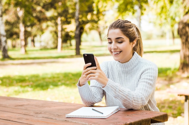 Ritratto di una bella donna digitando sullo smartphone in un parco in autunno.