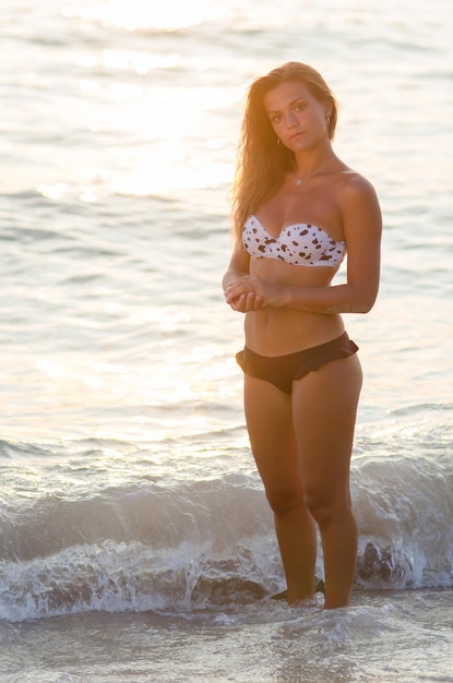 Ritratto di una bella donna fiduciosa in piedi al mare durante il tramonto