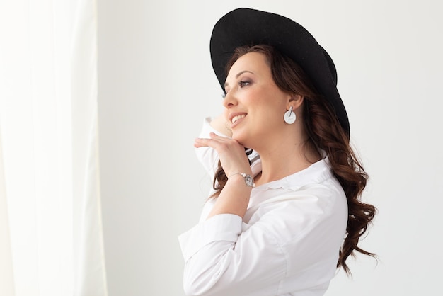 Ritratto di una bella donna graziosa in cappello elegante con un'ampia tesa su sfondo chiaro con copia