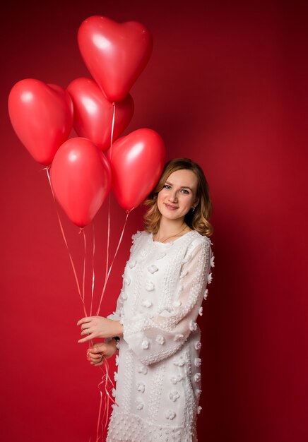 Ritratto di una bella donna in un abito bianco con palloncini a forma di cuore su un rosso