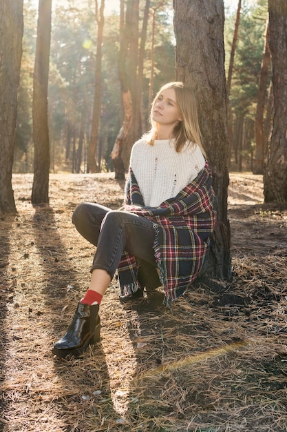 Ritratto di una bella donna premurosa che si appoggia su un albero in una foresta di pini