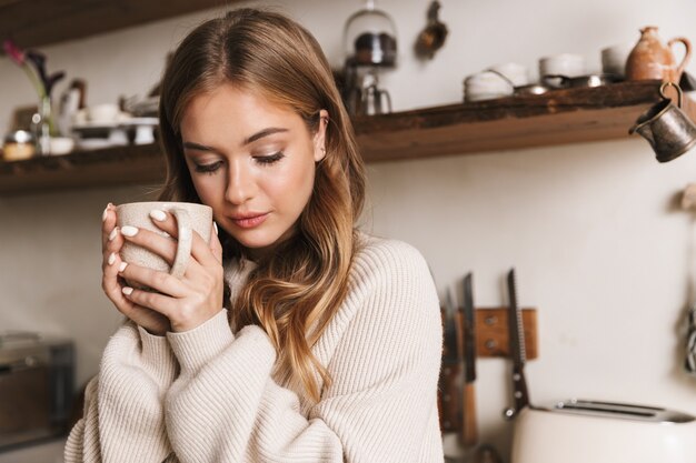 ritratto di una bella donna simpatica che indossa abiti casual che beve caffè e guarda verso il basso nell'accogliente cucina