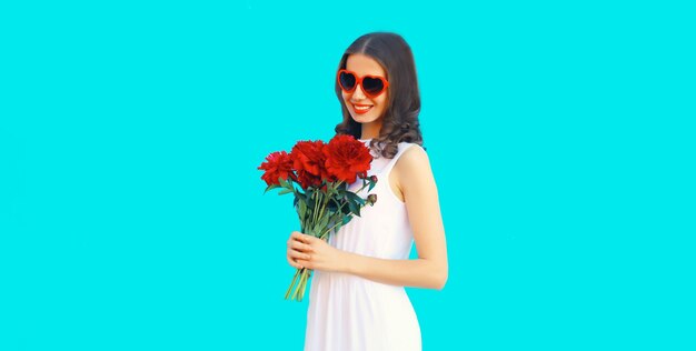 Ritratto di una bella donna sorridente con un bouquet di fiori di rosa rossa in occhiali da sole a forma di cuore