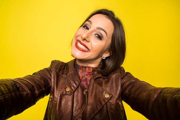Ritratto di una bella donna sorridente di successo che fa selfie su una parete gialla