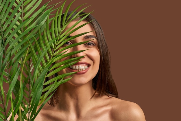 Ritratto di una bella donna su uno sfondo marrone che tiene un ramo di una palma e sorridente