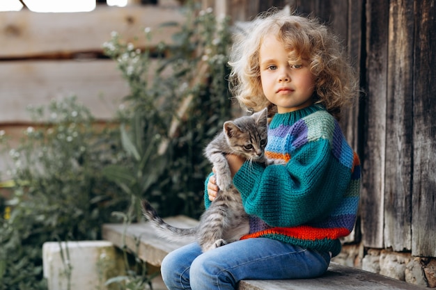 Ritratto di una bella e felice ragazza riccia in un maglione lavorato a maglia che gioca con un gattino vicino a una parete di legno