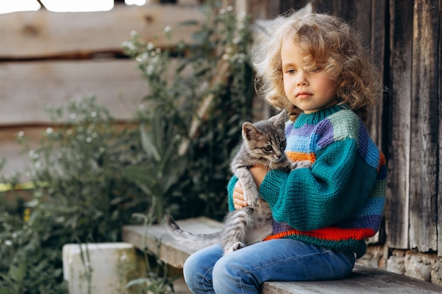 Ritratto di una bella e felice ragazza riccia in un maglione lavorato a maglia che gioca con un gattino vicino a una parete di legno