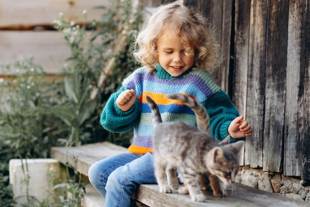 Ritratto di una bella e felice ragazza riccia in un maglione lavorato a maglia che gioca con un gattino vicino a una parete di legno