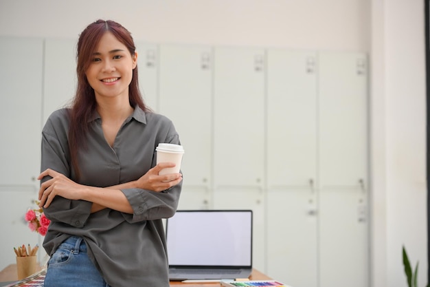 Ritratto di una bella giovane designer grafica femminile asiatica che si appoggia sul suo tavolo da lavoro in ufficio