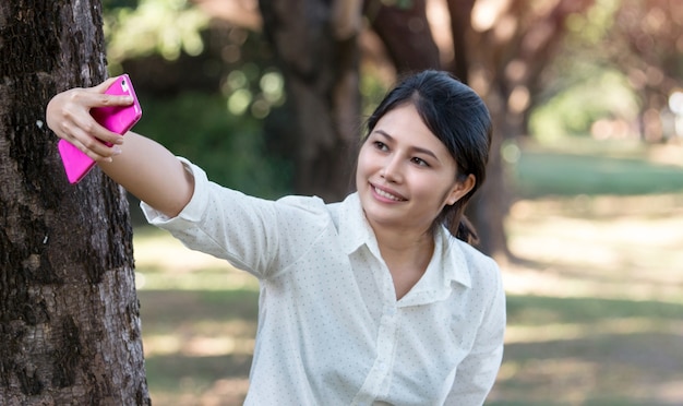 Ritratto di una bella giovane donna asiatica selfie nel parco con uno smartphone.