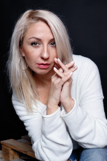 Ritratto di una bella giovane donna attraente in un maglione bianco con gli occhi azzurri e lunghi capelli biondi.