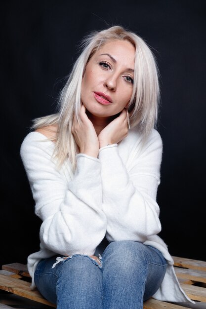 Ritratto di una bella giovane donna attraente in un maglione bianco con gli occhi azzurri e lunghi capelli biondi.