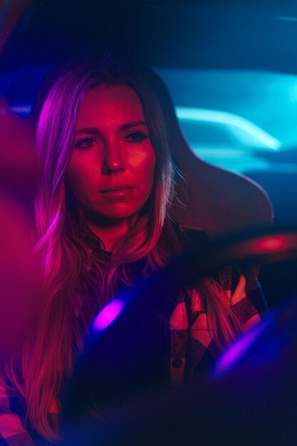 Ritratto di una bella giovane donna che guida una macchina di notte alla luce del neon