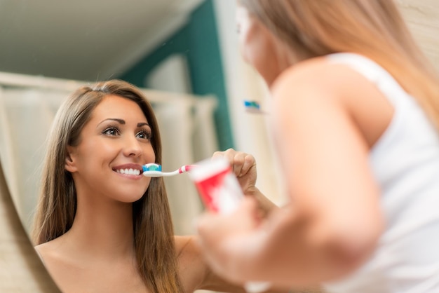 Ritratto di una bella giovane donna che pulisce i denti davanti al suo specchio del bagno. Messa a fuoco selettiva.