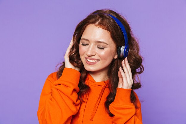 Ritratto di una bella giovane donna dai capelli rossi in piedi su viola, ascoltando musica con le cuffie
