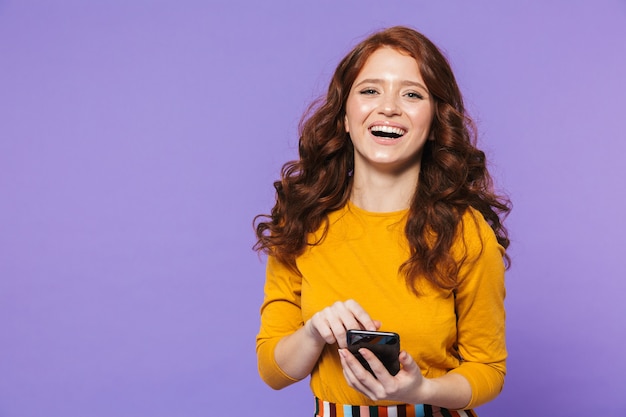 Ritratto di una bella giovane donna dai capelli rossi in piedi su viola, utilizzando il telefono cellulare, indicando