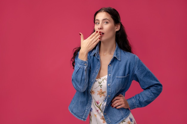 Ritratto di una bella giovane donna in abito leggero e camicia blu in piedi su sfondo rosa in borchie...