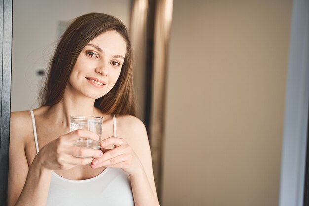 Ritratto di una bella giovane donna moderna sorridente con un bicchiere d'acqua che guarda avanti