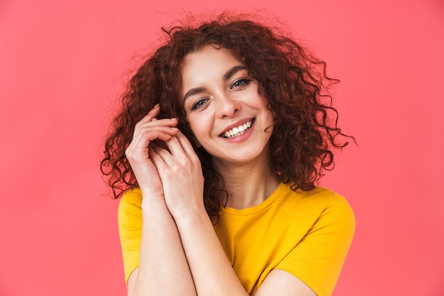 Ritratto di una bella giovane donna riccia felice carina in posa isolata sulla parete rossa.