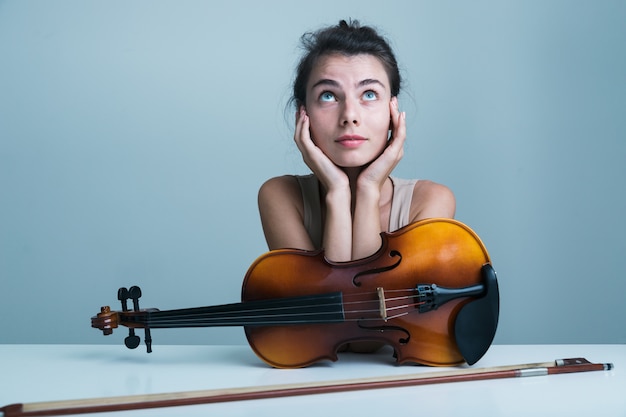 Ritratto di una bella giovane donna seduta al tavolo con un violino isolato su sfondo blu