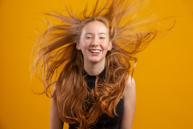 Ritratto di una bella ragazza allegra rossa con i capelli battenti sorridendo ridendo sul muro giallo