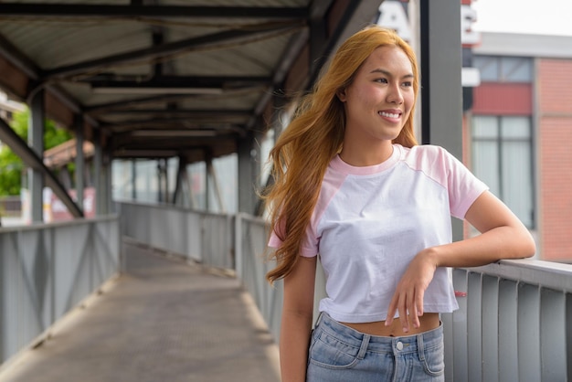 Ritratto di una bella ragazza asiatica con i capelli biondi che sorride e pensa all'aperto