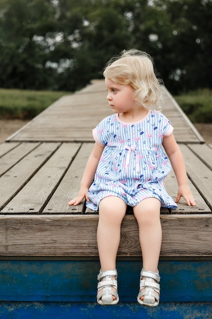 Ritratto di una bella ragazza bionda seduta su un pantone in legno. Foto di alta qualità