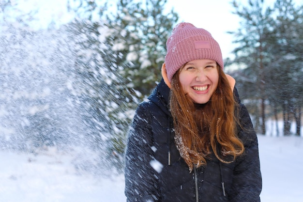 Ritratto di una bella ragazza carina nel parco o nella foresta all'aperto donna che si diverte ridendo sorridendo all'adolescente della natura in un panno caldo Bufera di neve e fiocchi di neve che cadono