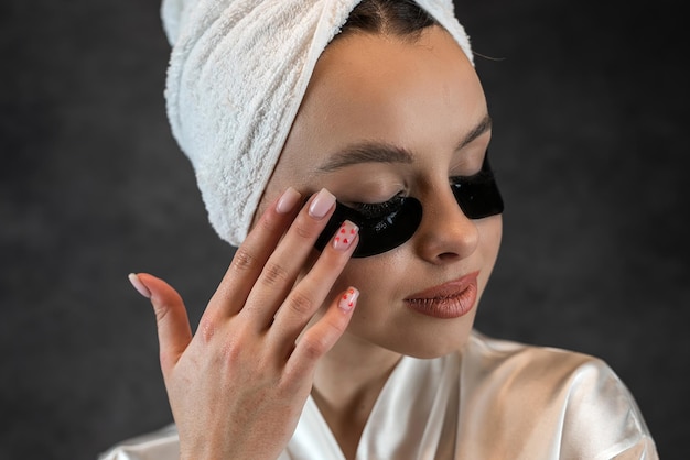Ritratto di una bella ragazza caucasica con un cerotto di idrogel di collagene applicato sotto l'occhio isolato su nero