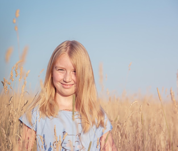 Ritratto di una bella ragazza con i capelli dorati in una maglietta blu in un campo con erba secca su sfondo blu cielo Copia spazio per testo Immagine tinta