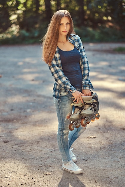 Ritratto di una bella ragazza con i capelli lunghi che indossa una maglietta in pile e jeans, tiene i rulli, in piedi in una campagna.