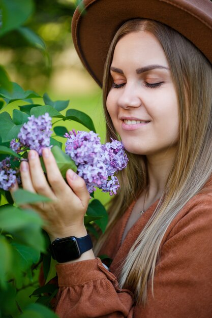 Ritratto di una bella ragazza con un cappello marrone con un lillà in giardino