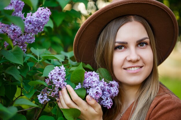 Ritratto di una bella ragazza con un cappello marrone con un lillà in giardino