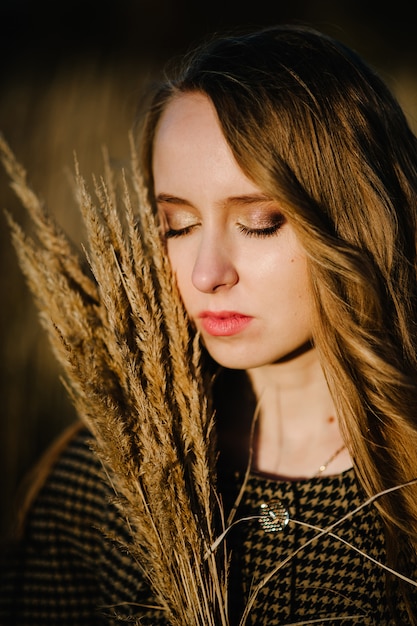 Ritratto di una bella ragazza con un mazzo di erba secca in autunno in un'erba alta e lunga sulla natura. mezza lunghezza superiore. Avvicinamento. colpo alla testa.