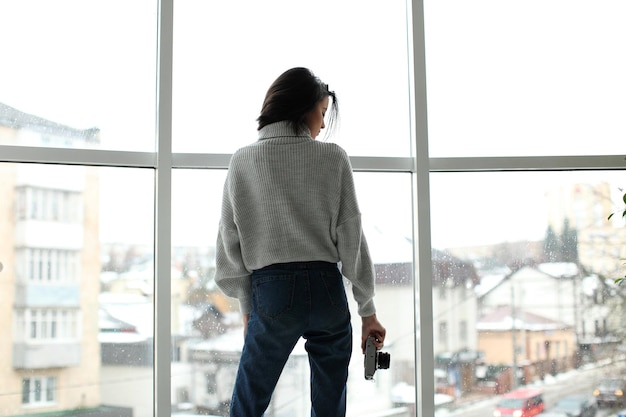 Ritratto di una bella ragazza con una macchina fotografica in piedi vicino alla finestra