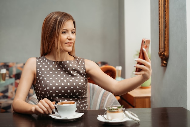 Ritratto di una bella ragazza dai capelli castani che fa selfie sul suo telefono cellulare al tavolo del ristorante