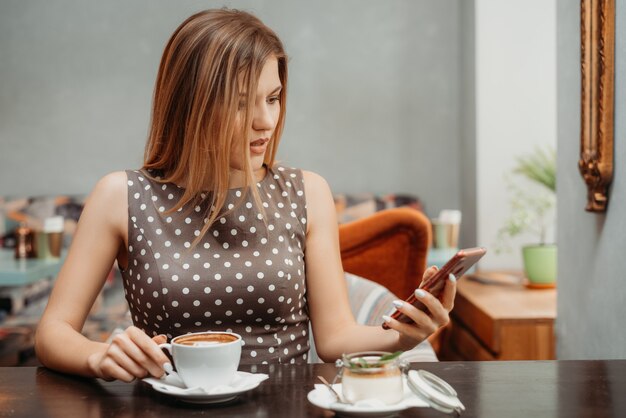 Ritratto di una bella ragazza dai capelli castani con gli occhi aperti che legge qualcosa sul suo telefono cellulare al tavolo del ristorante