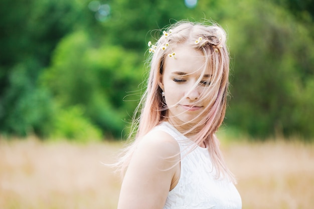 Ritratto di una bella ragazza dai capelli rosa con una ghirlanda di margherite nel campo