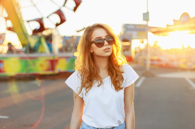 Ritratto di una bella ragazza dai capelli rossi in occhiali da sole al tramonto.