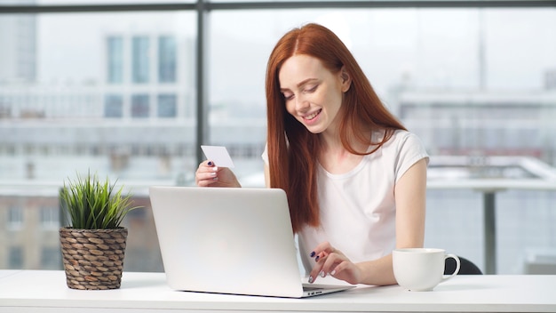 Ritratto di una bella ragazza di successo rossa lavorando a un computer, a una scrivania in ufficio